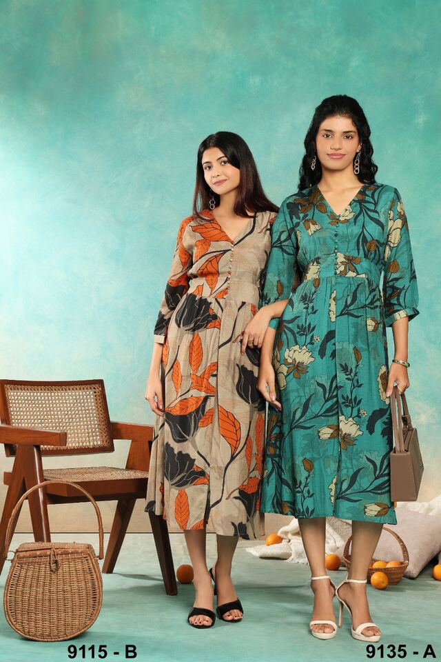 Two women in botanical-print midi dresses beside a cane chair against a painted teal wall