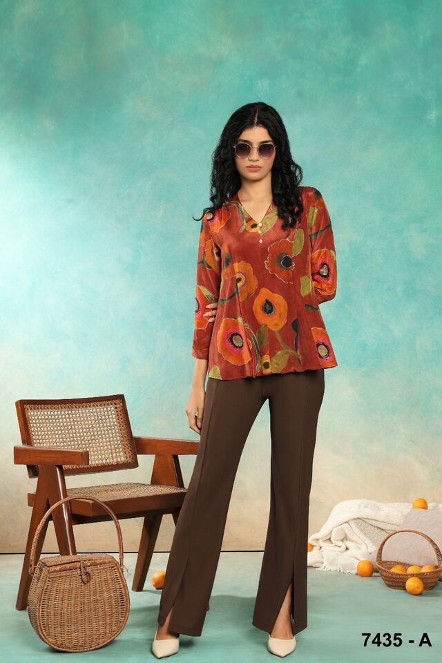 Bold orange floral blouse with split-hem brown trousers against a teal backdrop